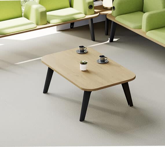 Table basse ILOT en bois clair avec pieds noirs, entourée de fauteuils verts, deux tasses et une plante posées dessus.