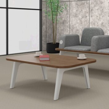 Table basse ILOT en bois avec pieds blancs, entourée de fauteuils gris, un livre et deux tasses posés dessus.