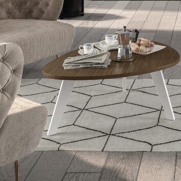 Table basse en forme de galet, avec un plateau en bois foncé et des pieds blancs, sur un tapis géométrique.