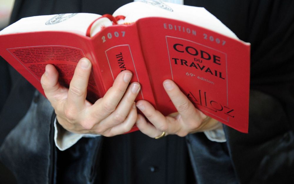 Personne tenant ouvert le Code du Travail français édition 2007, livre de référence juridique rouge